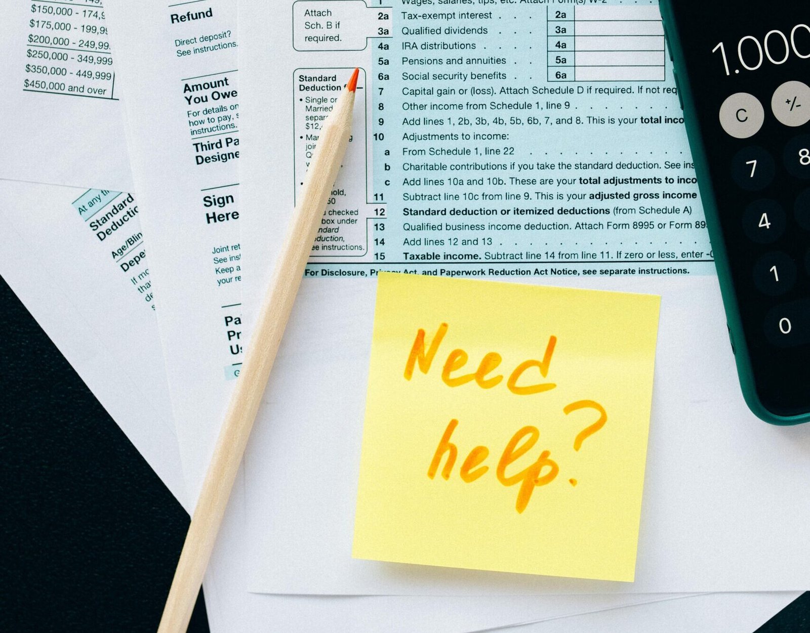Close-up of tax forms with a calculator and a note asking for assistance.